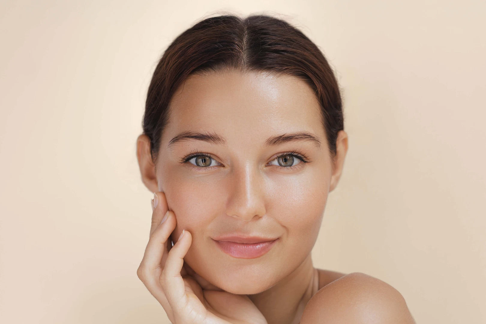 A young woman with a clear complexion smiling while touching her cheek.