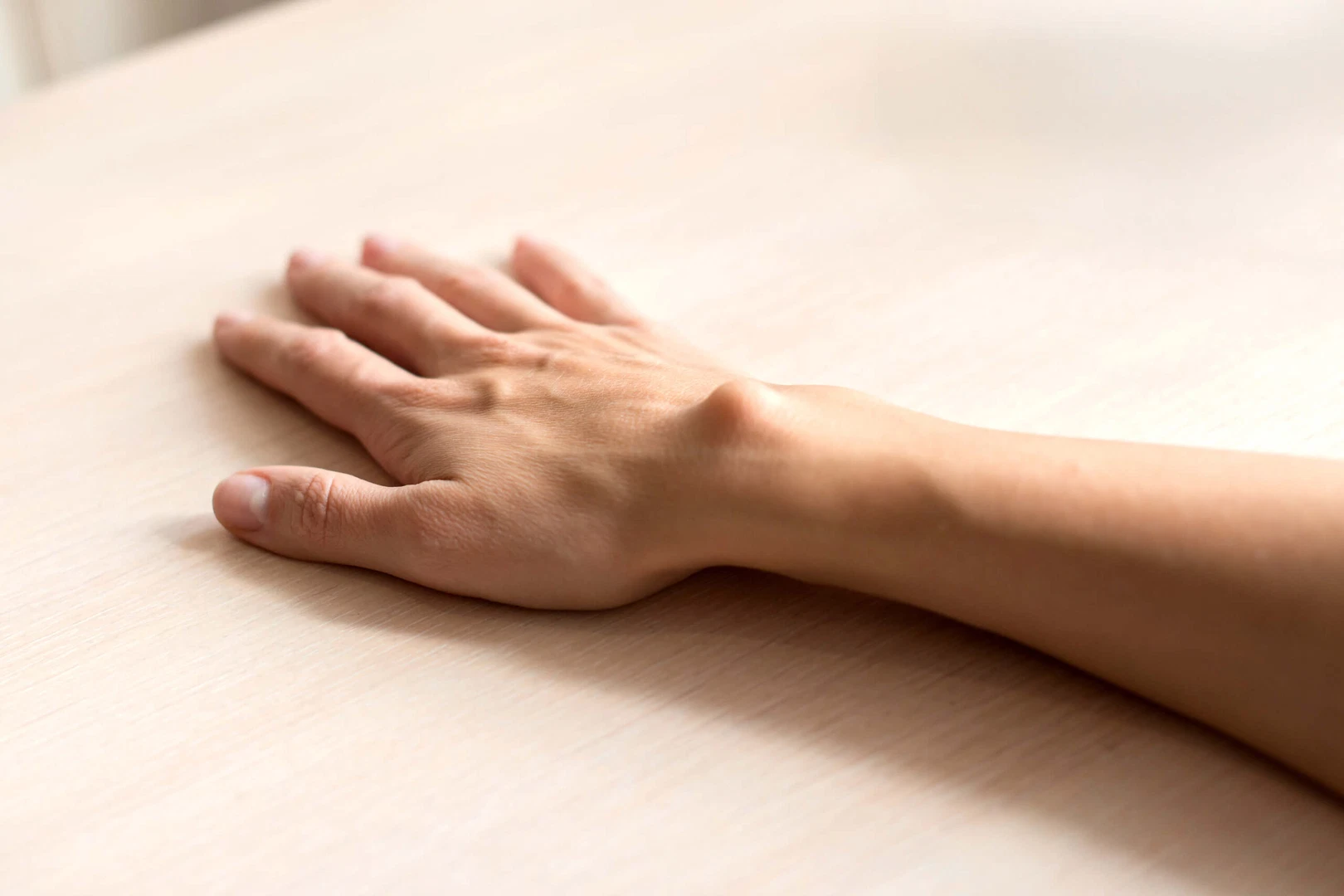 A close-up of a patient's hand and wrist resting on a table with a visible lipoma or cyst.